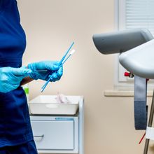 health care provider standing in front of gynecology stirrups holding swabs for Pap smear